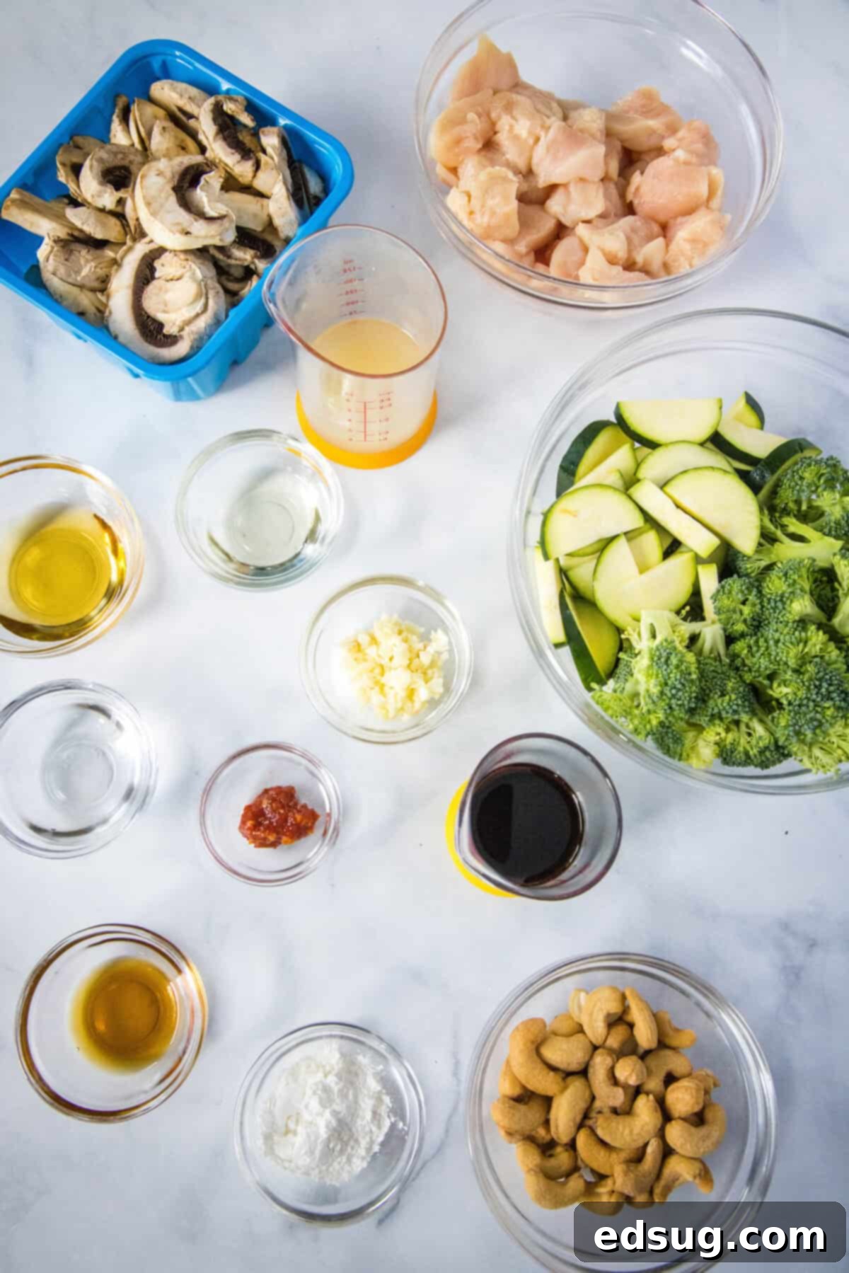best chicken stir fry ingredients laid out on a cutting board, including chicken breast, fresh broccoli, zucchini, mushrooms, garlic, and cashews