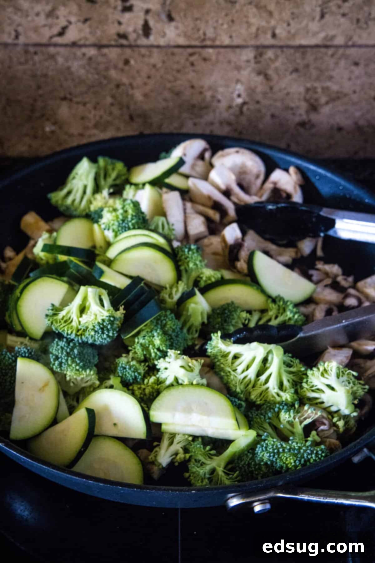 fresh vegetables cooking in a hot skillet, including broccoli, zucchini, and mushrooms, starting to brown