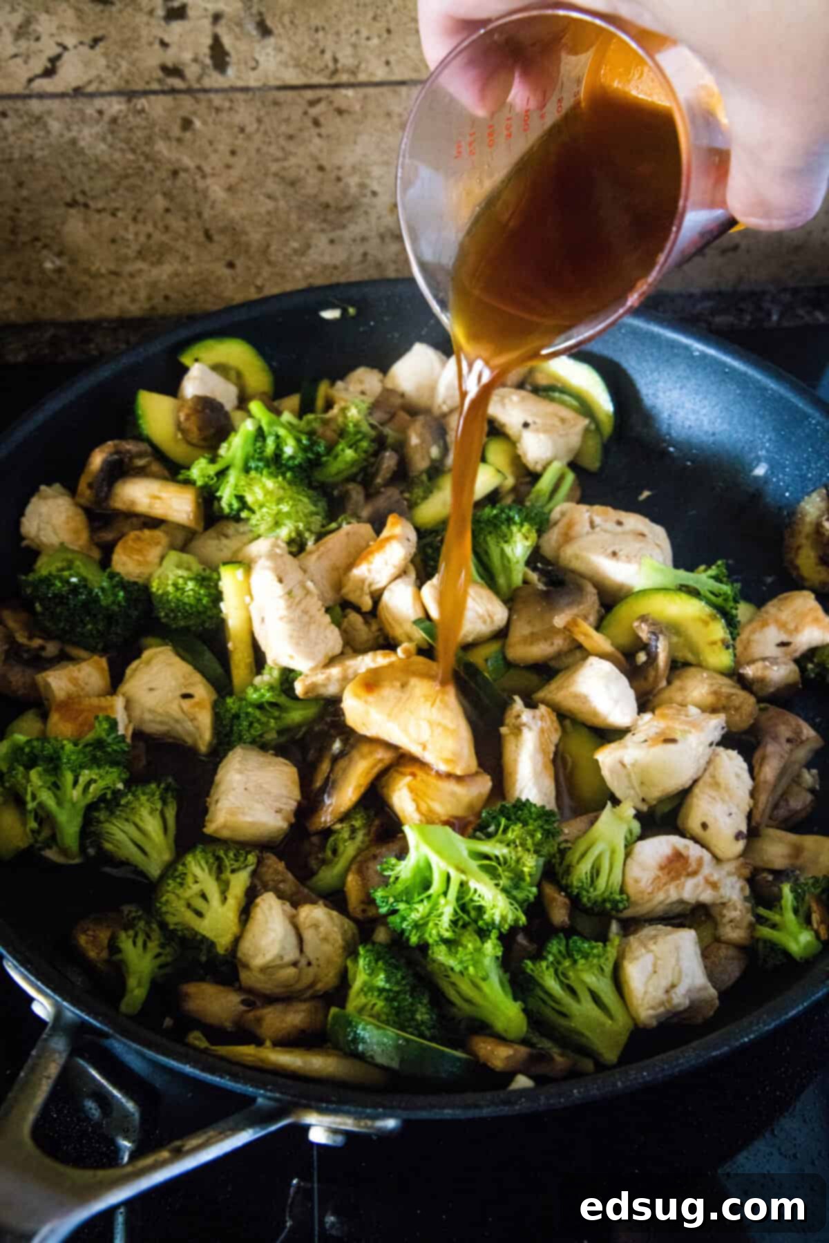 pouring stir fry sauce into skillet over cooked chicken and vegetables, creating a rich, glossy coating