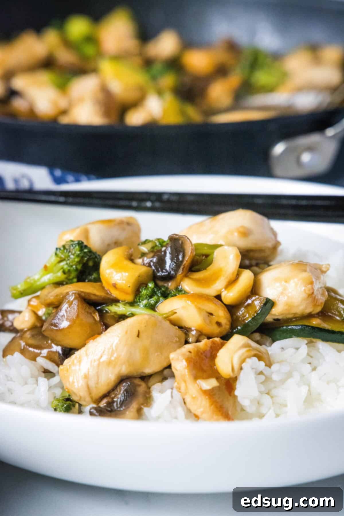 chicken stir fry served over rice in a bowl, garnished with sesame seeds and green onions