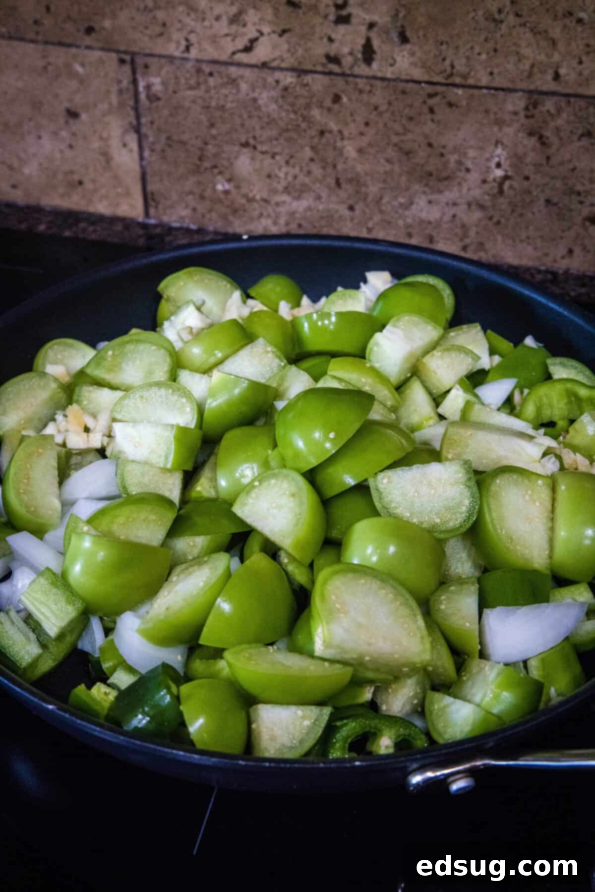 Authentic Green Enchilada Sauce 4 Adding chopped tomatillos, peppers, onion, and garlic to a hot skillet with olive oil to begin cooking the ingredients for green enchilada sauce.