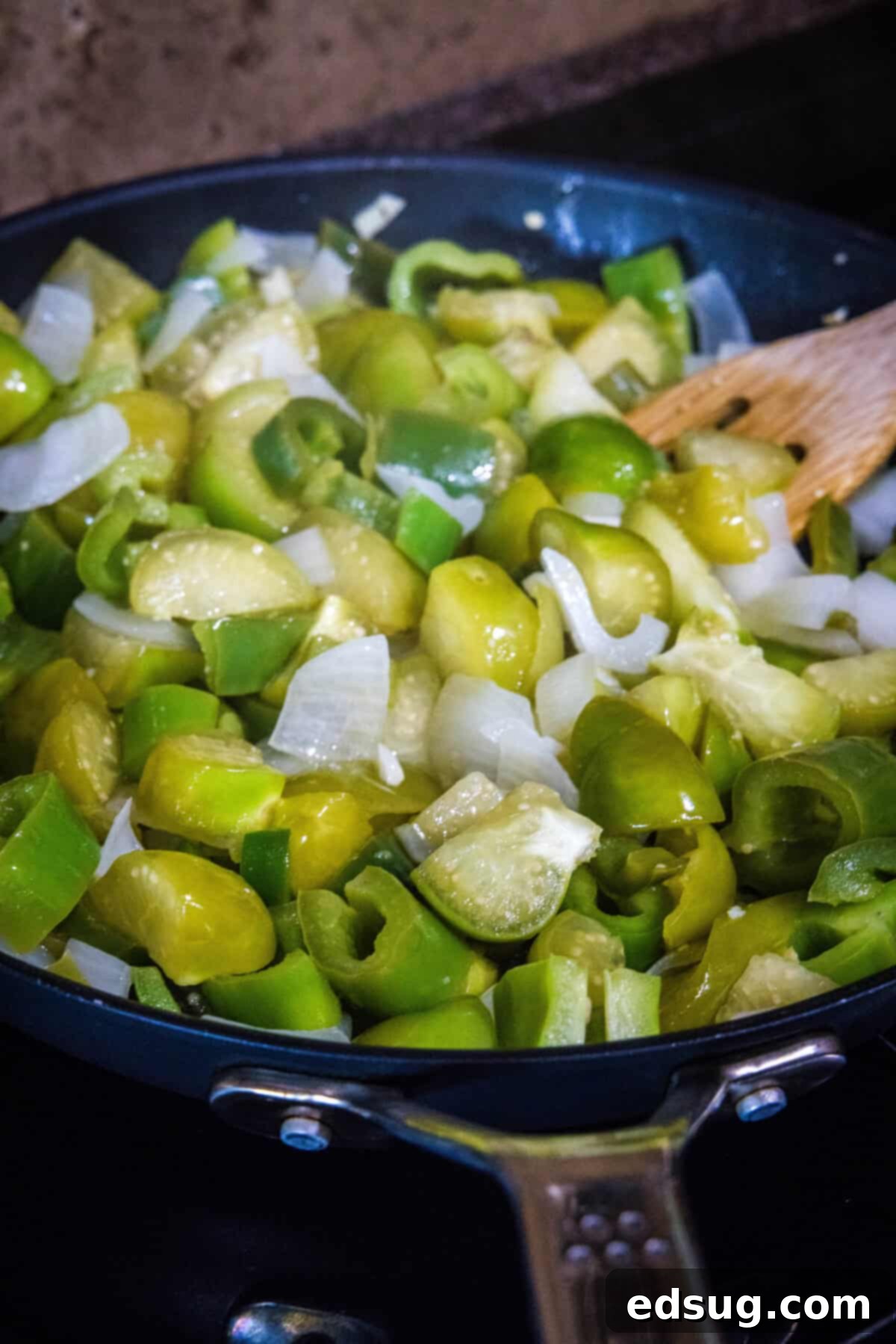 Authentic Green Enchilada Sauce 5 A close-up view of chopped vegetables, including tomatillos, green peppers, onion, and garlic, gently simmering in a pan on the stovetop, softening for the enchilada sauce.