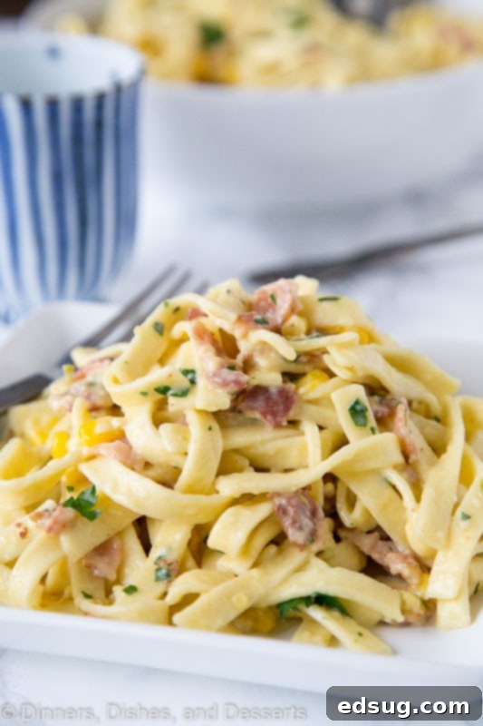 Fiesta Carbonara 3 A beautifully plated portion of creamy carbonara pasta, garnished with fresh corn, crispy bacon, and finely chopped green chilies, served on a white plate