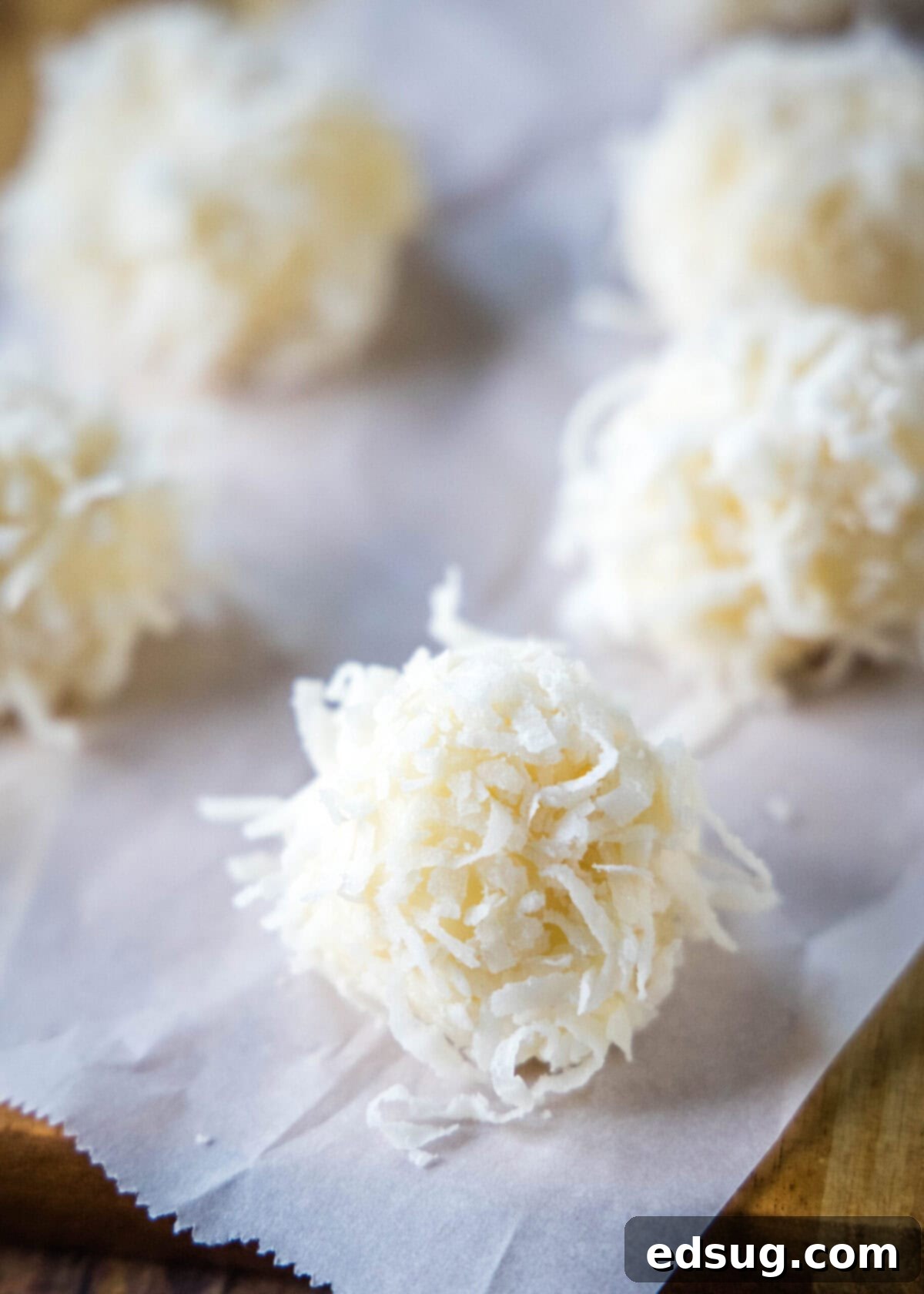 White chocolate truffles covered in coconut on a piece of parchment paper, ready to be served
