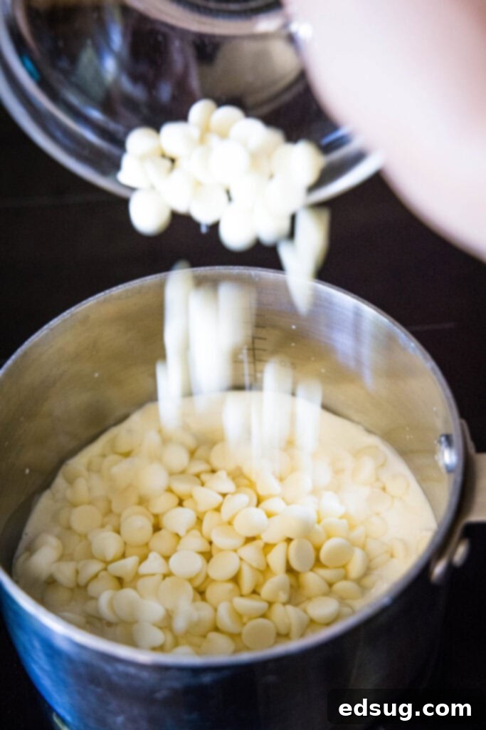 White chocolate chips being poured into a saucepan with warm cream