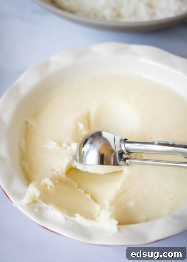 A cookie scoop forming balls of white chocolate truffle mixture from a chilled bowl