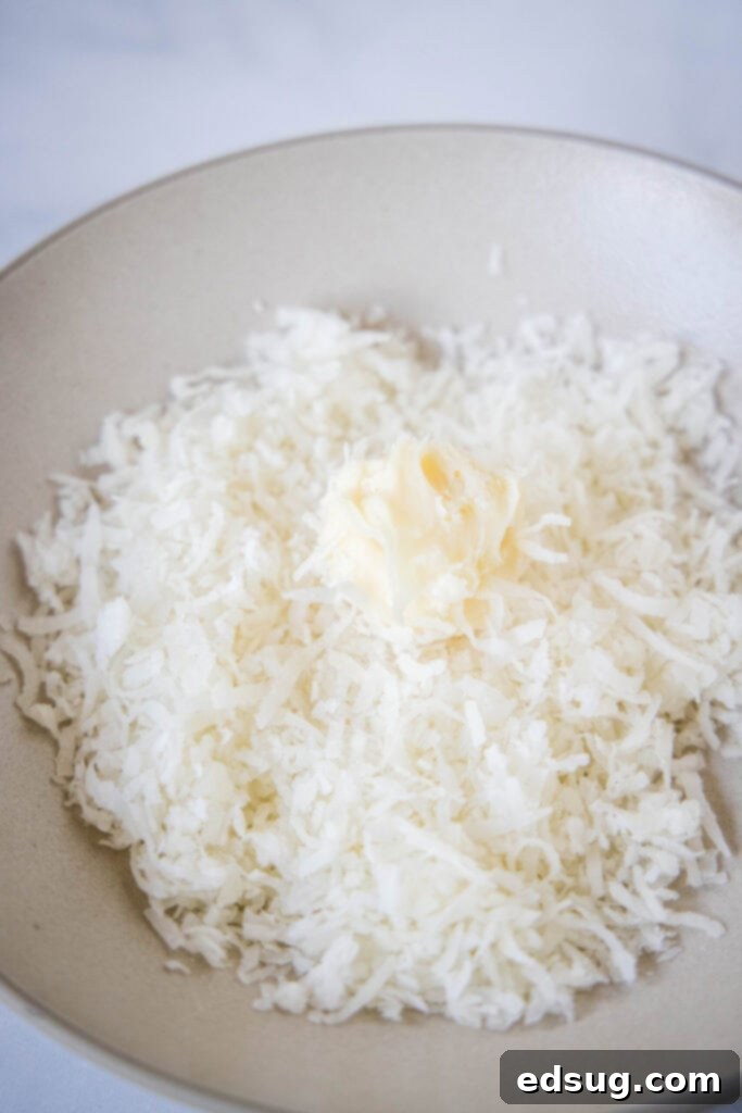 A freshly scooped white chocolate truffle being rolled in a bowl of shredded coconut