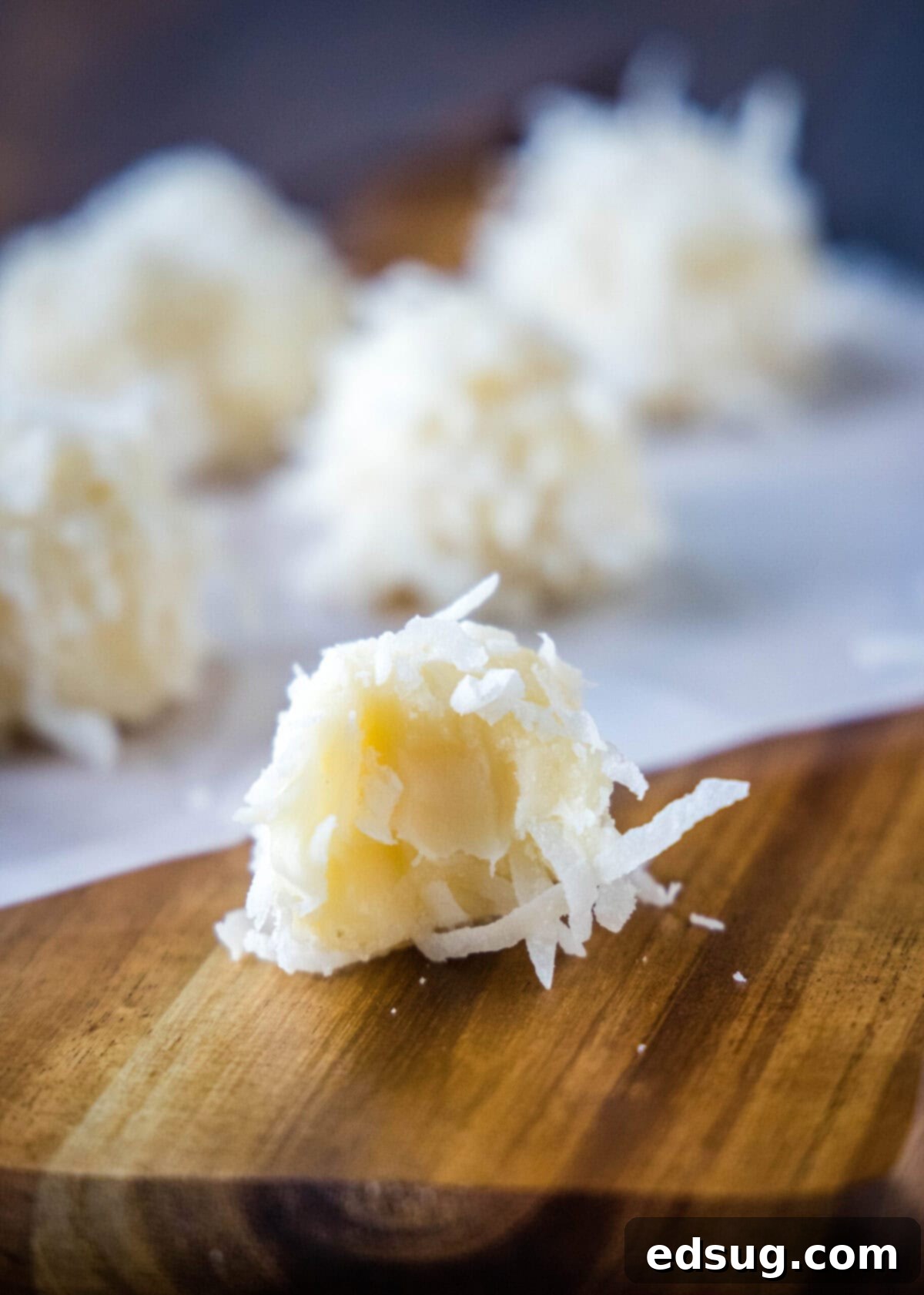 A half-eaten white chocolate coconut truffle with more truffles in the background, showcasing the creamy interior and coconut coating