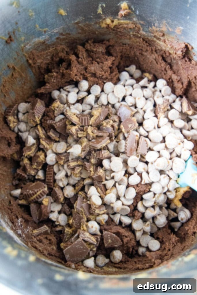 Cookie dough with peanut butter chips and chopped mini peanut butter cups ready to be folded in, showcasing the rich texture before baking.