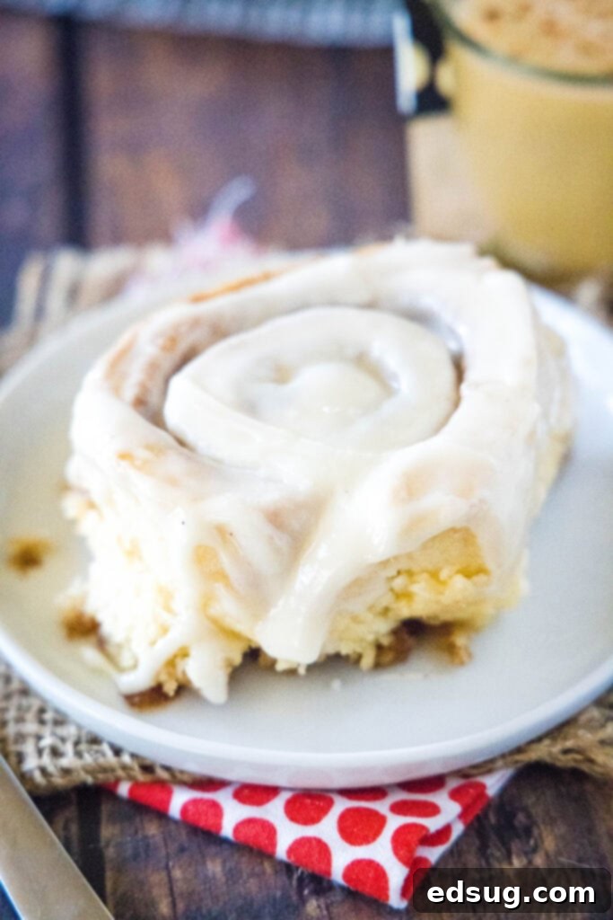 Festive Eggnog Cinnamon Rolls 5 single eggnog cinnamon roll on a white plate, showing the rich icing and soft texture.