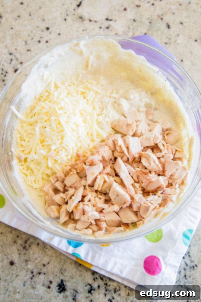 Southwest Green Chile Chicken Enchilada Dip 3 A mixing bowl filled with all the delicious ingredients for green chili chicken enchilada dip before baking, showing the creamy texture and chicken pieces.