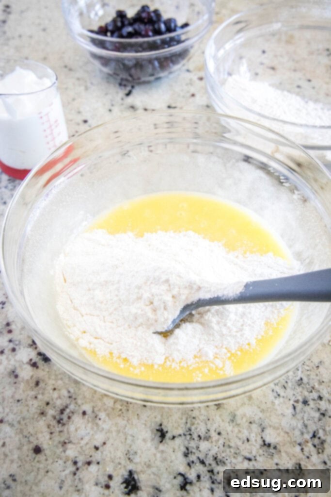 A close-up shot of flour being added to the lemon cake batter, showing the creamy texture.