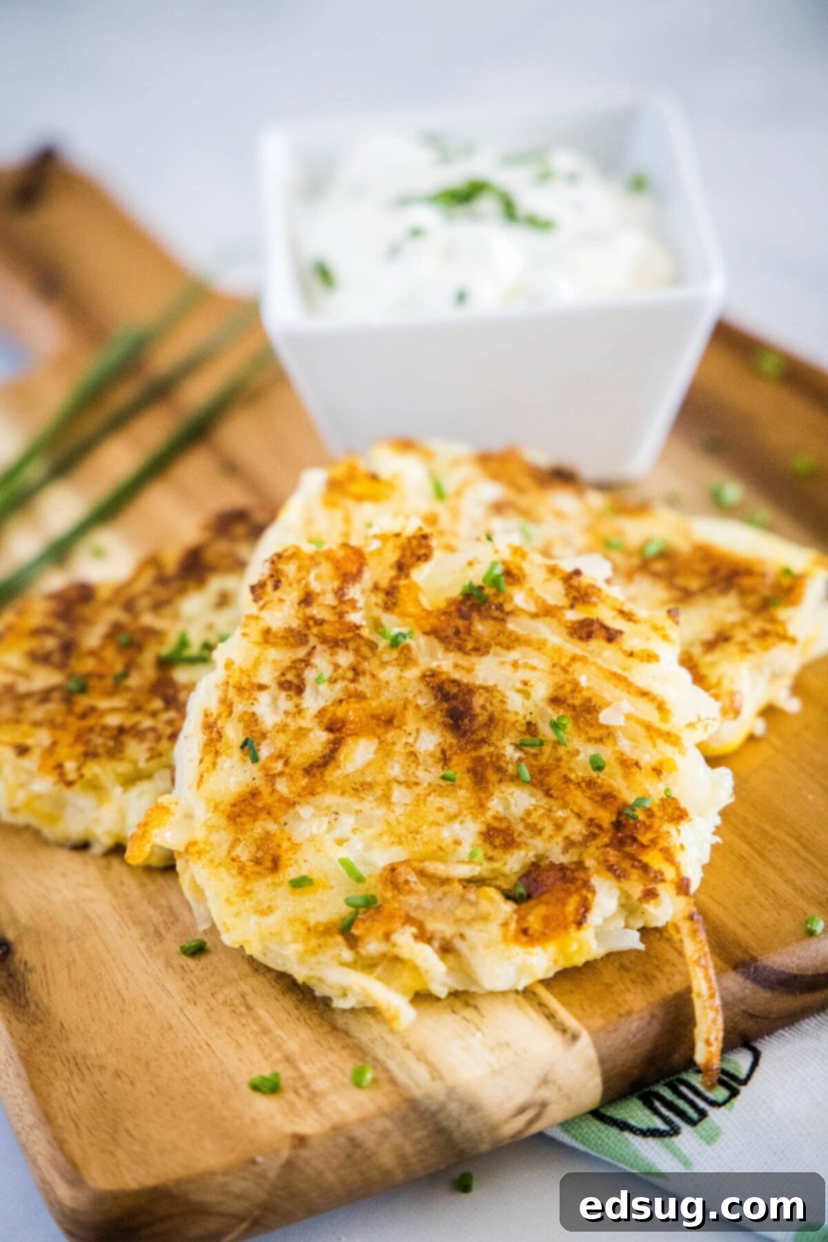 These easy cauliflower fritters are packed with hash browns and cheddar cheese, and served with a creamy and tart dipping sauce. Close up of cauliflower fritters on a cutting board with a bowl of sauce behind them