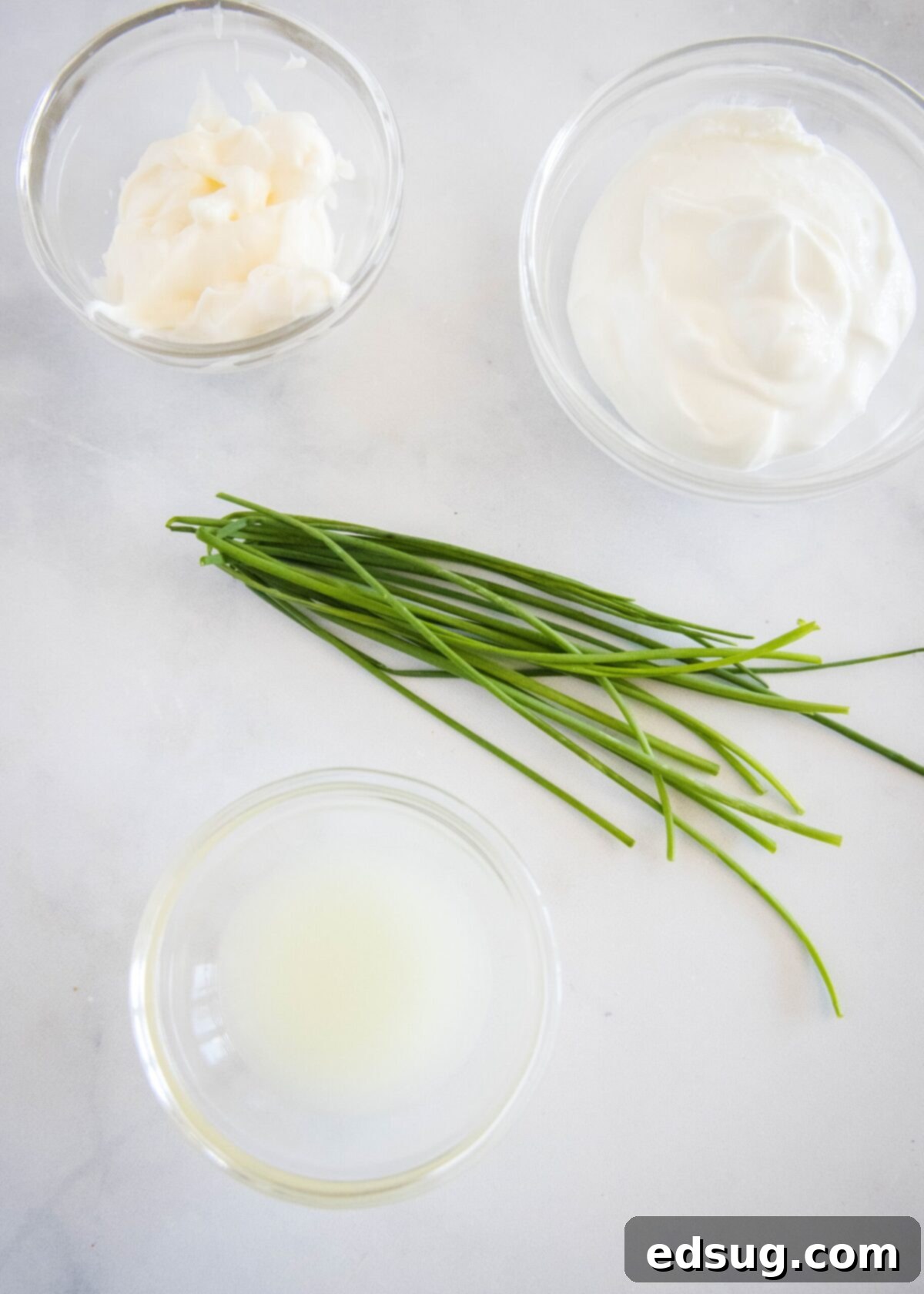 These easy cauliflower fritters are packed with hash browns and cheddar cheese, and served with a creamy and tart dipping sauce. Overhead view of the ingredients needed for a dipping sauce: a handful of chives, a bowl of lemon juice, a bowl of mayo, and a bowl of Greek yogurt