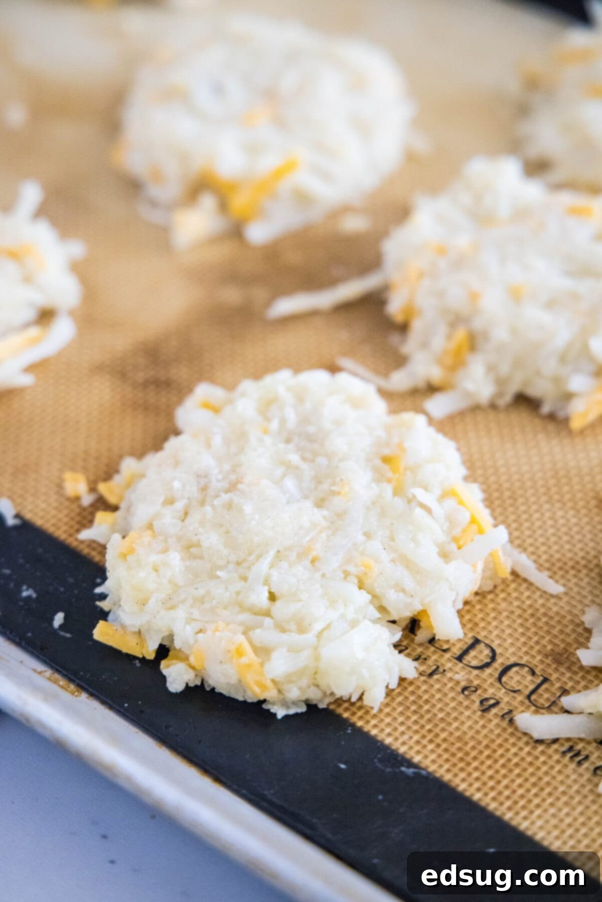 These easy cauliflower fritters are packed with hash browns and cheddar cheese, and served with a creamy and tart dipping sauce. Portioned cauliflower fritters, uncooked, on a baking sheet