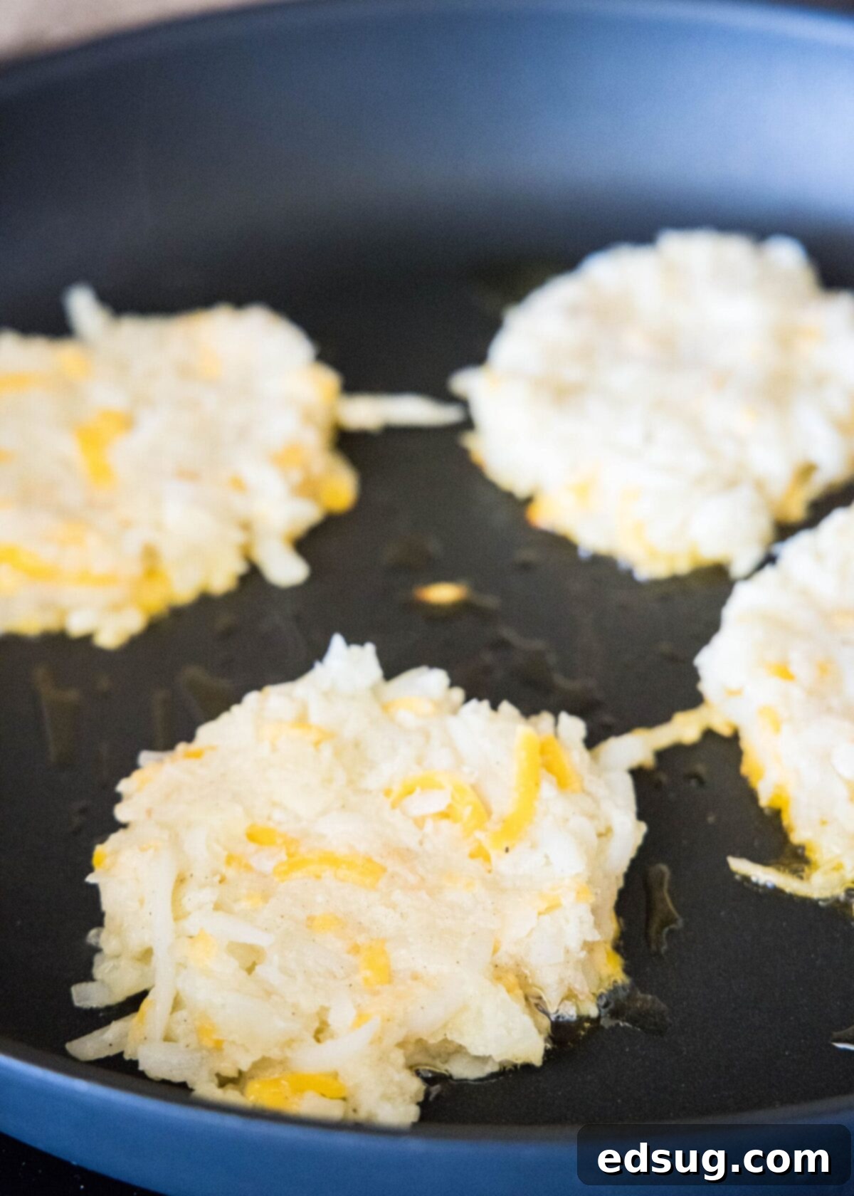 Four uncooked cauliflower fritters in a skillet