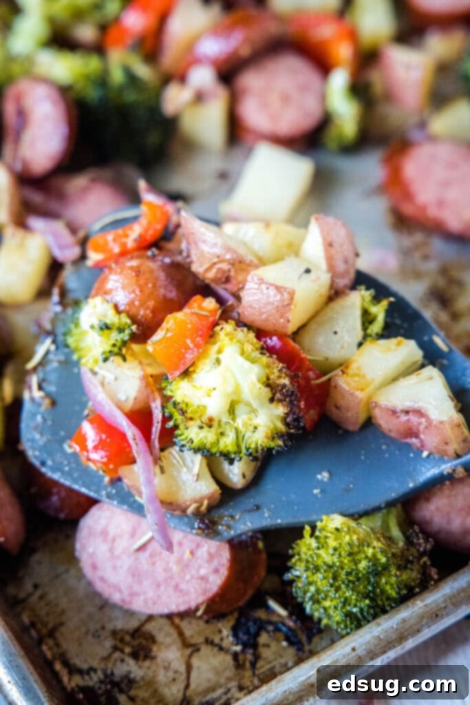 Flavorful One-Pan Sausage and Potatoes 2 A close-up shot of perfectly roasted potatoes, sausage, and vegetables being scooped from a sheet pan with a spatula, highlighting their crispy texture and vibrant colors.