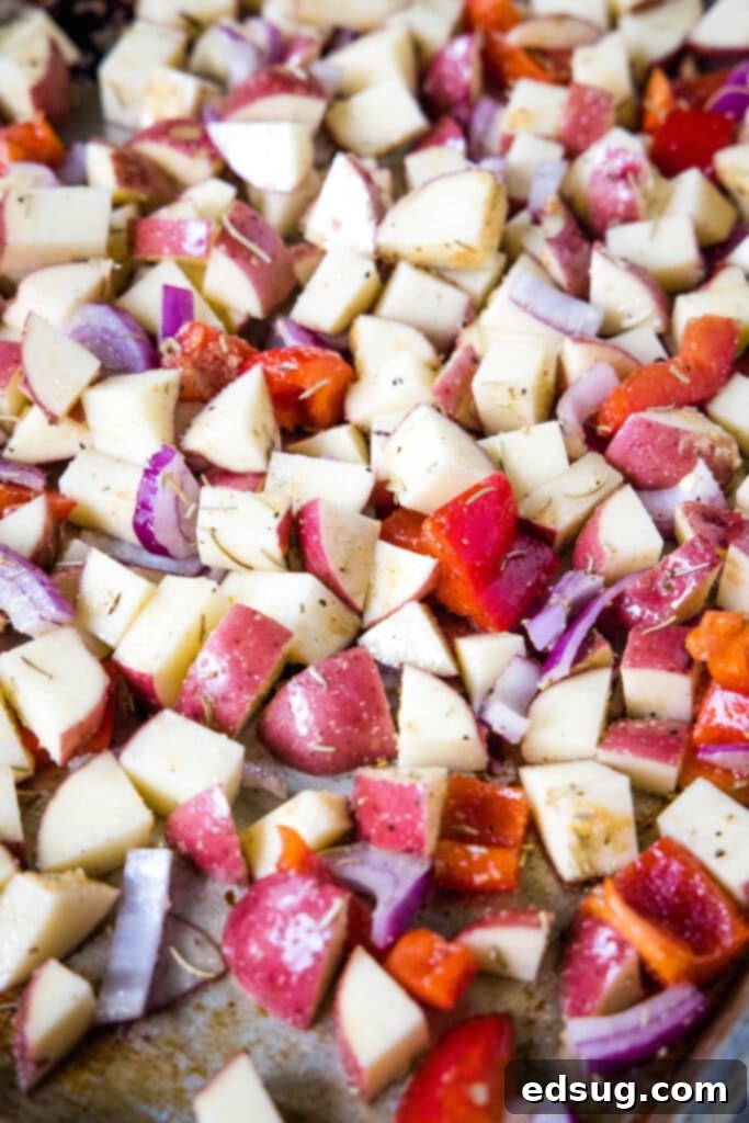 Flavorful One-Pan Sausage and Potatoes 4 Chopped red potatoes, onion, and bell peppers evenly spread on a large baking sheet, ready for the first stage of roasting.