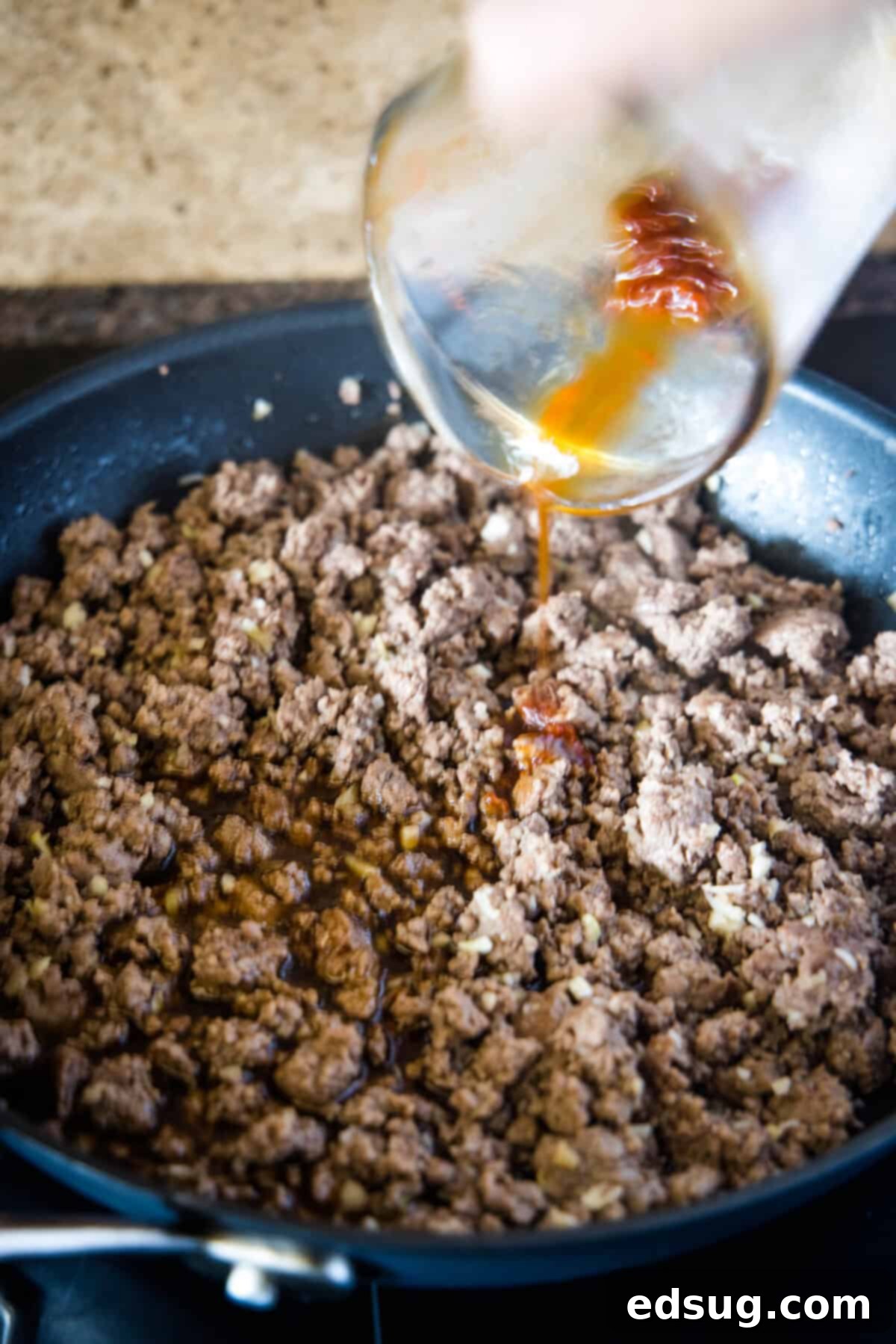 adding sauce to beef in a skillet